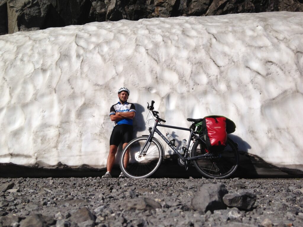 Paul with his loaded touring bike next to a wall of snow, July 2013