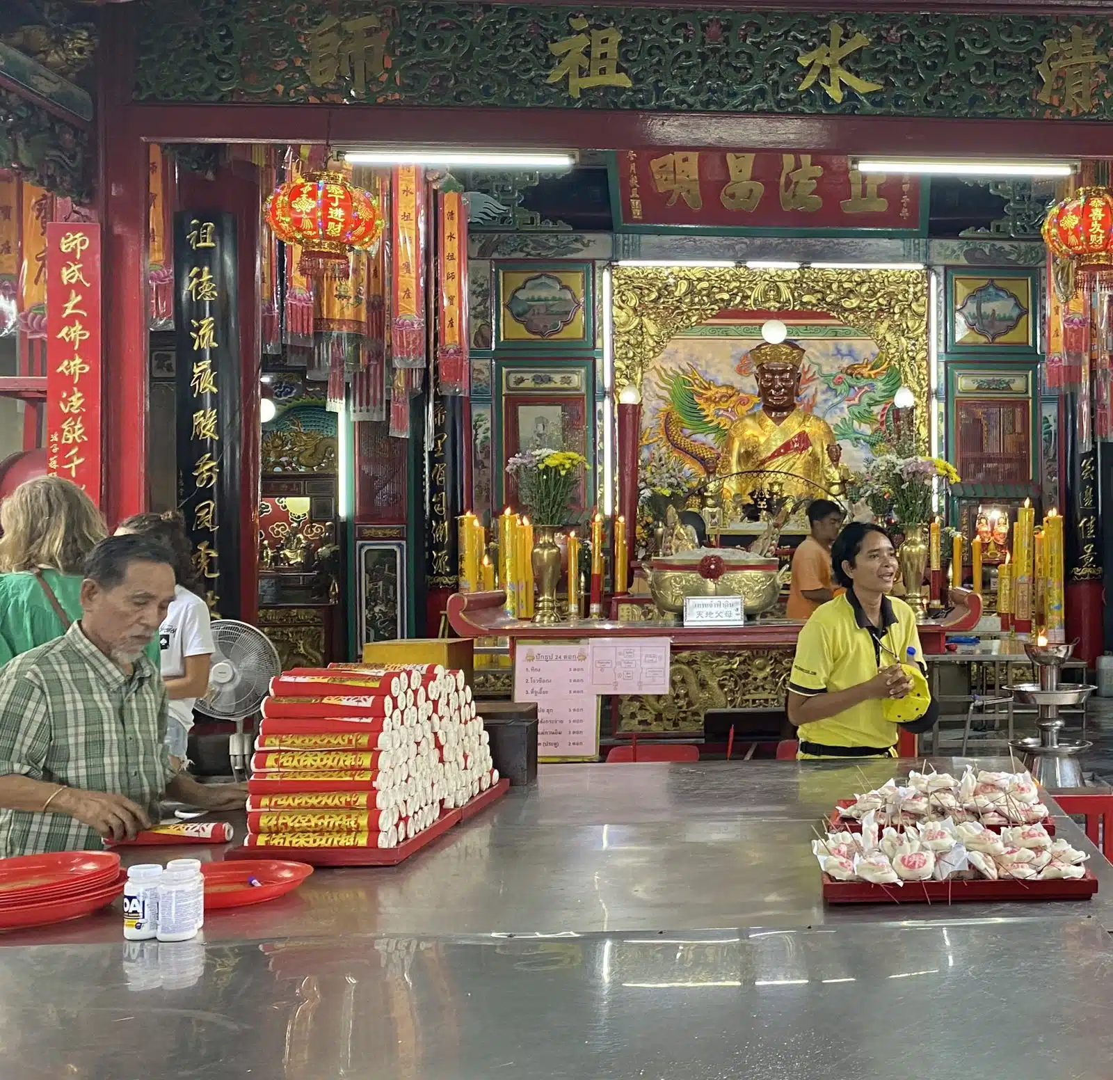 Inside a Chinese shrine in Talat Noi with offerings and a guide in a yellow Co van Kessel shirt