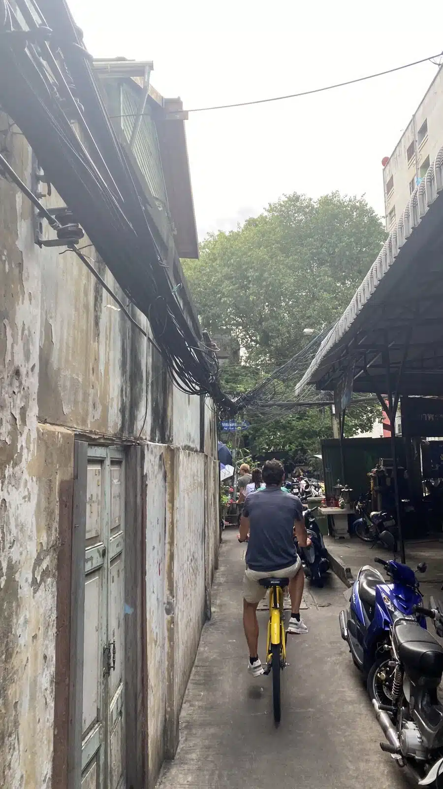 Cyclists on yellow city bikes riding through an old alley in Talat Noi, Bangkok
